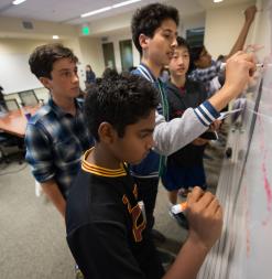 Participants work together, writing on a whiteboard.