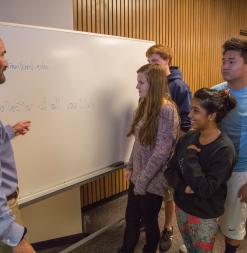 Students speak with their instructor at the whiteboard.